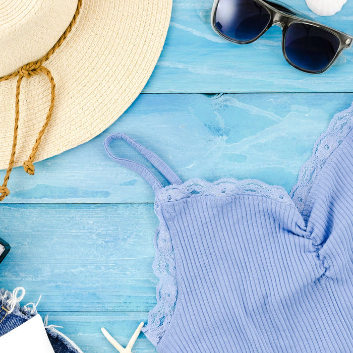 Vintage summer outfit featuring a blue tank top, straw hat, sunglasses, and a retro camera on a blue wooden background.