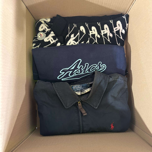 A cardboard box containing folded branded clothing items, including a Moncler sweater, an Asics jacket, and a Polo Ralph Lauren shirt.