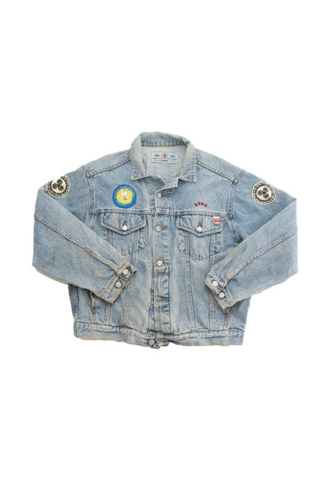 Vintage blue denim jacket with unique patches on the sleeves and chest laying flat.